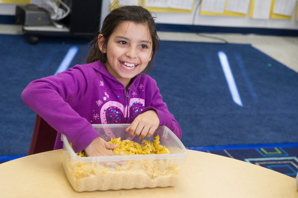 Girl putting hand in tub of noodles. Photograph by Jeff Woodward.