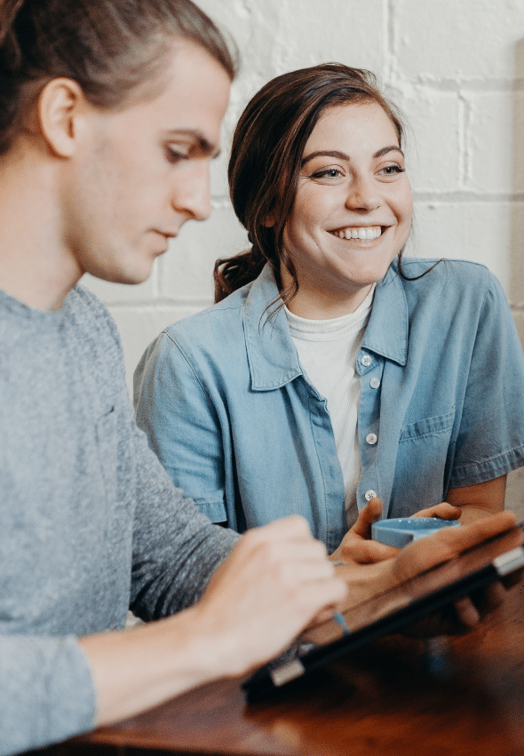 A smiling woman at a desk next to a man taking notes