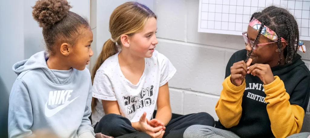 Three elementary school students sit and share with one another.