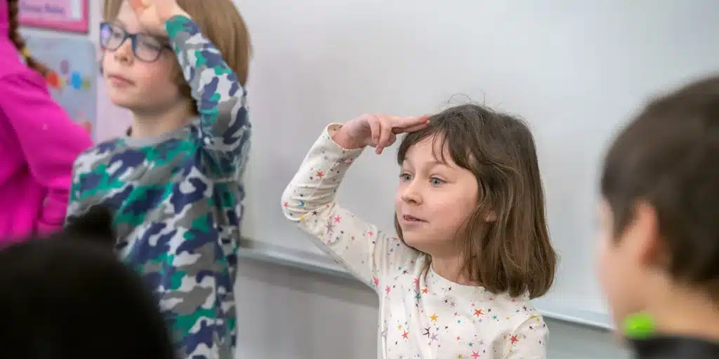 Excited students in a class, playing the Still As A Rock Energizer, hold their hands to their heads while trying to remain still.