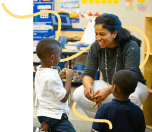 An elementary school teacher smiles while talking to two students