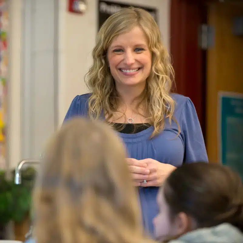A middle school teacher smiles happily at students in her class